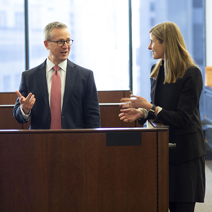 Male and female BBHer standing and talking at office workstation