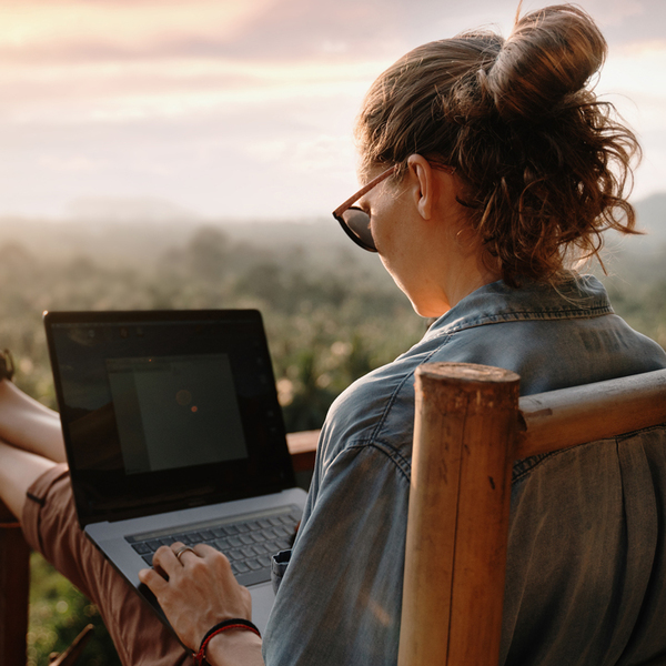 Young female working at a laptop at sunset or sunrise on the top of the mountain to the sea, working day.
