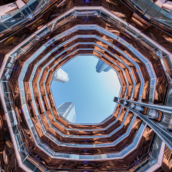 Hudson Yards wavy, modern structure taken from down below with a blue sky seen from the top and skyscrapers looming above