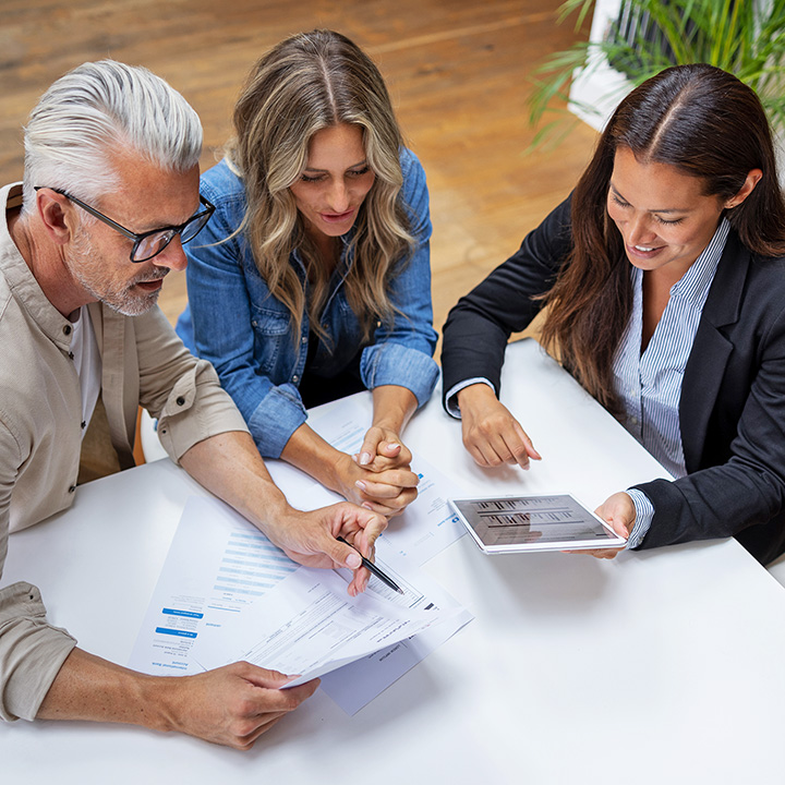 Three people gathered around a tablet discussing financial charts.