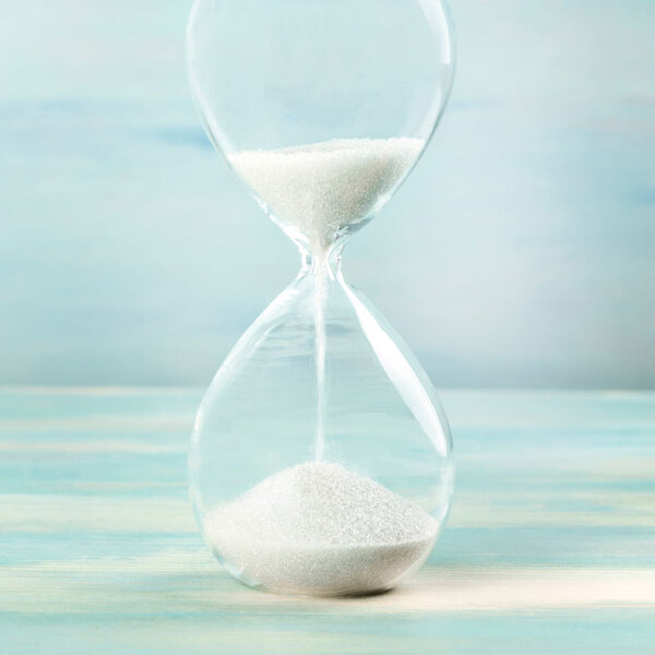 A side view of an hourglass with falling sand on a teal background 