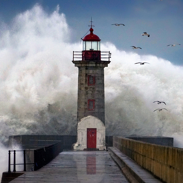 Large wave crashing behind a lighthouse