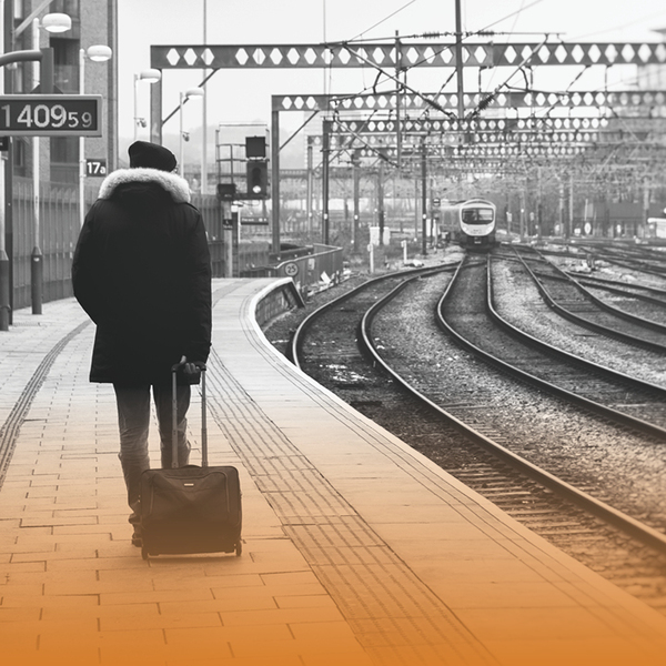 Black and white image of a man pulling his hand luggage across a train platform