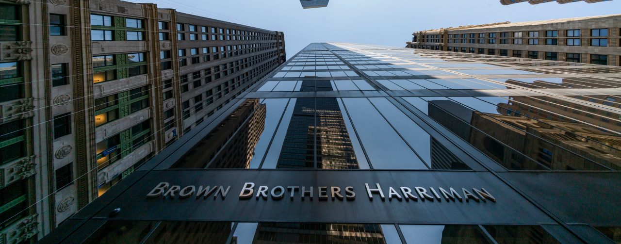 Brown Brothers Harriman building taken from down below with skyscrapers surrounding and a clear blue sky