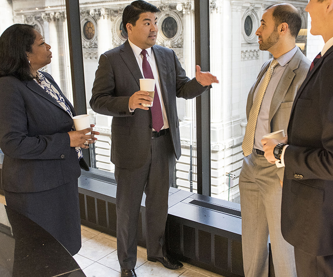 4 BBH employees having a discussion over coffee standing near windows