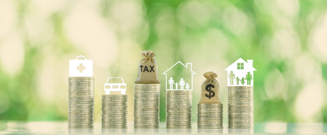 Family tax benefit, inherit tax, property or estate and household tax concept : Tax bag, family with kids living in a residential facility, a dollar bag, a car, a first aid kit are atop coin stacks.