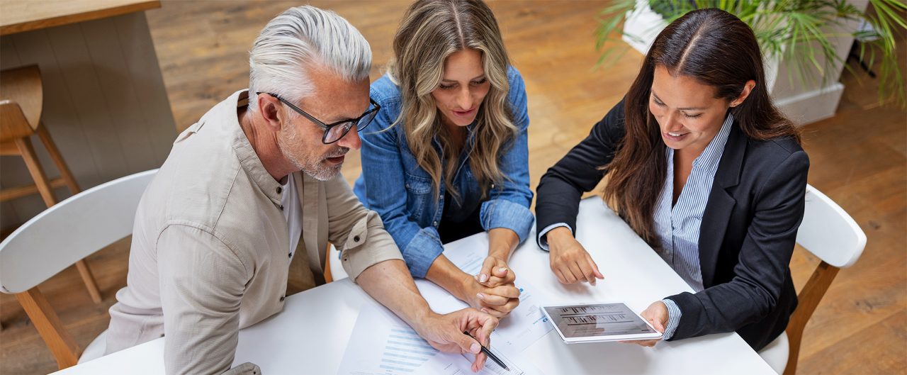 Three people gathered around a tablet discussing financial charts.