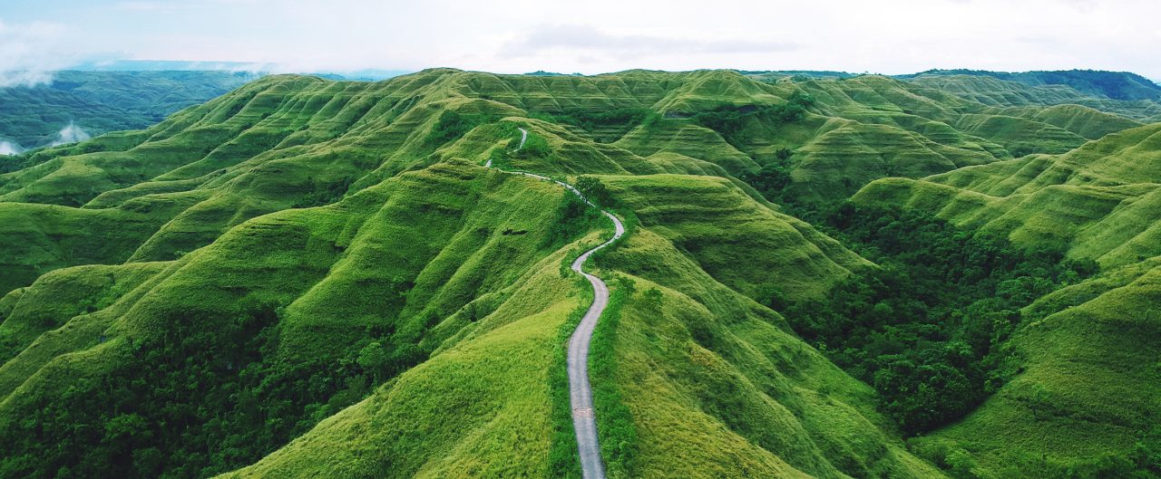 Aerial drone view: A long winding road between hills of green grass in remote parts of the Indonesian island of Sumba