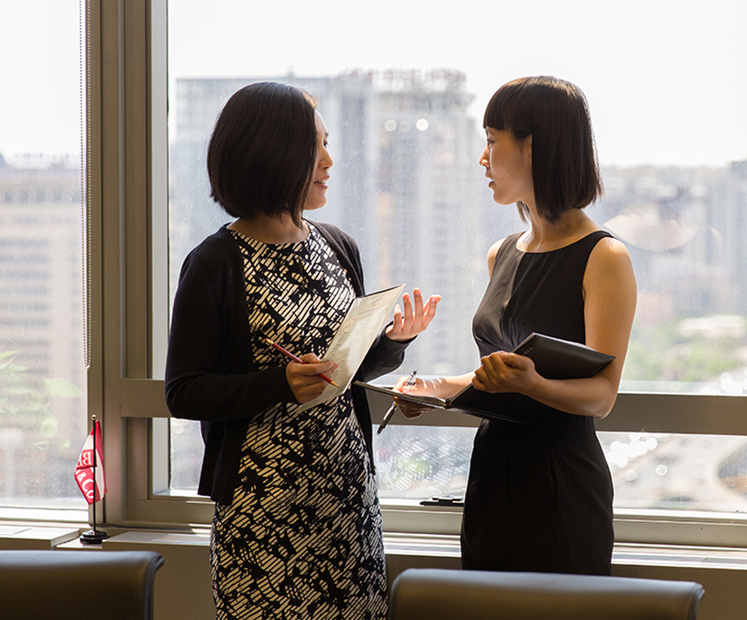 Two female employees talking near a window.